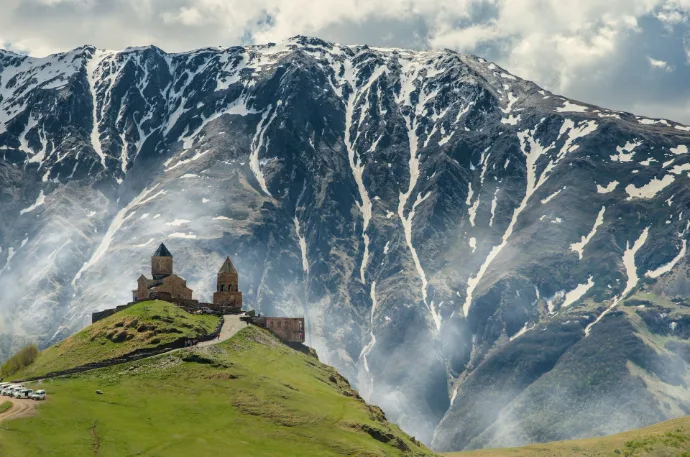 Gergeti Trinity Church on a green hill before a snow-capped mountain in Georgia
