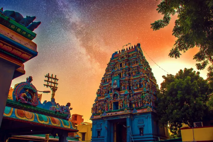 A colorful Hindu temple tower beneath a starry night sky with orange light